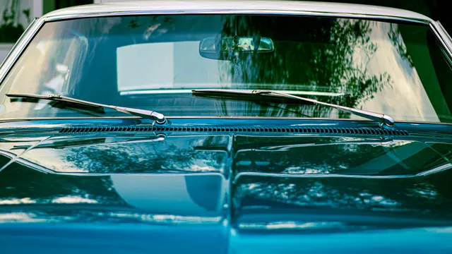 A vehicle windshield and wiper blades seen across the hood