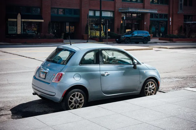 A light blue Fiat 500 parked on a city street