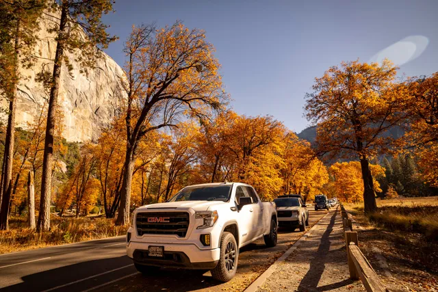 A GMC pickup truck on a road lined with autumn trees